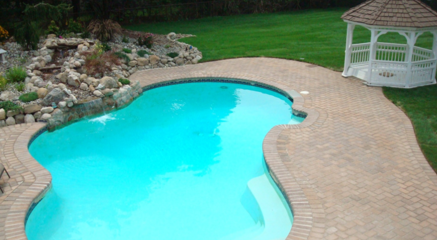 Swimming pool with waterfall feature and gazebo in green yard.