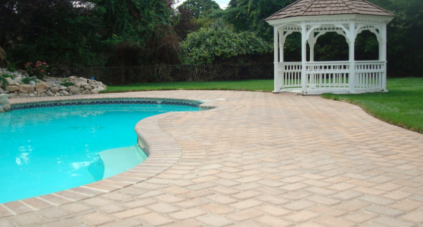 Swimming pool with stone patio, white gazebo, and green lawn.
