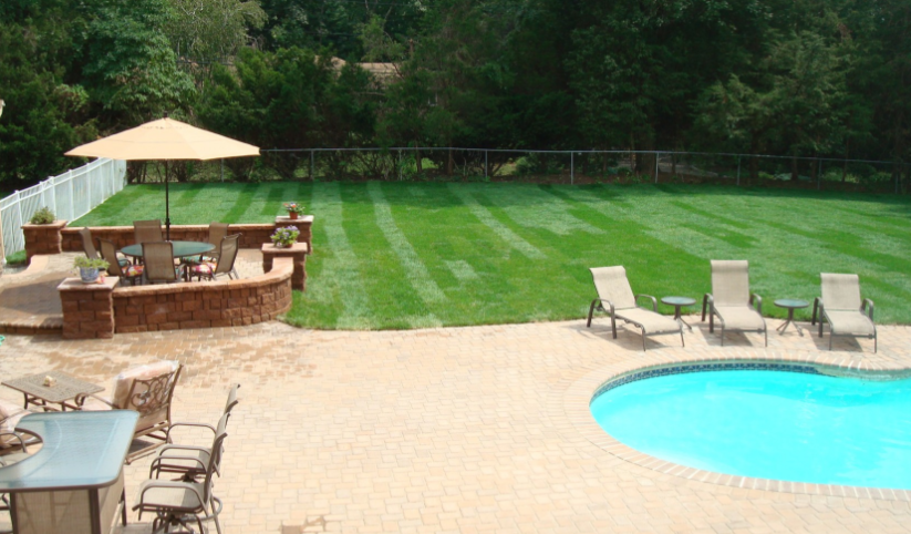 Backyard patio with pool, lawn, and seating area. Brick, tan, green, and blue.
