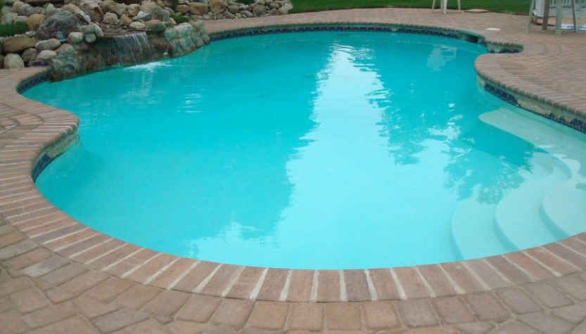 Swimming pool with brick border, light blue water, and small waterfall feature.