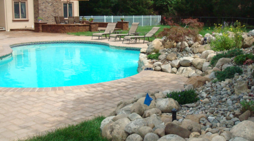 Backyard pool with stone landscaping, lounge chairs, and house in the background.