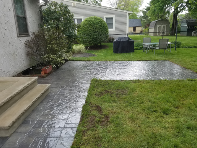 Backyard patio with stamped gray concrete, grass, and house.