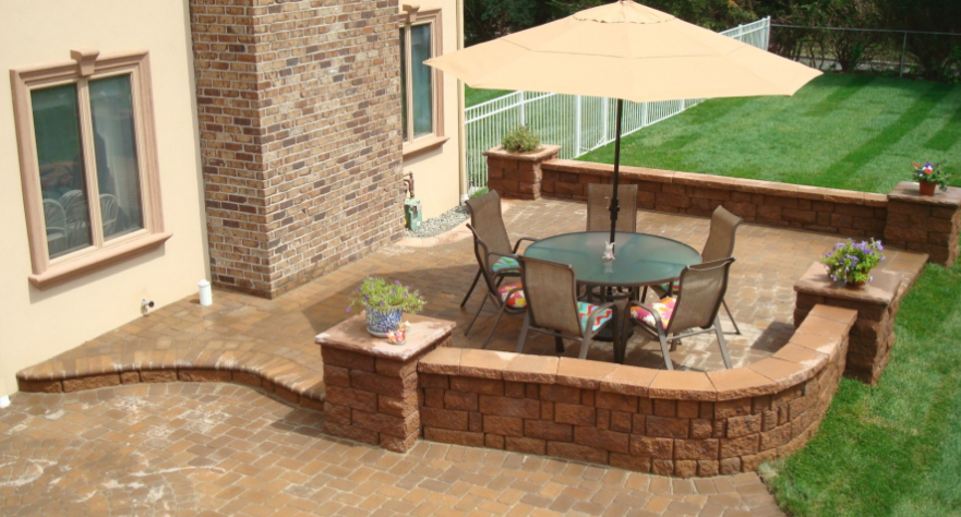 Patio with round table, chairs, and umbrella, surrounded by brick walls and green lawn.