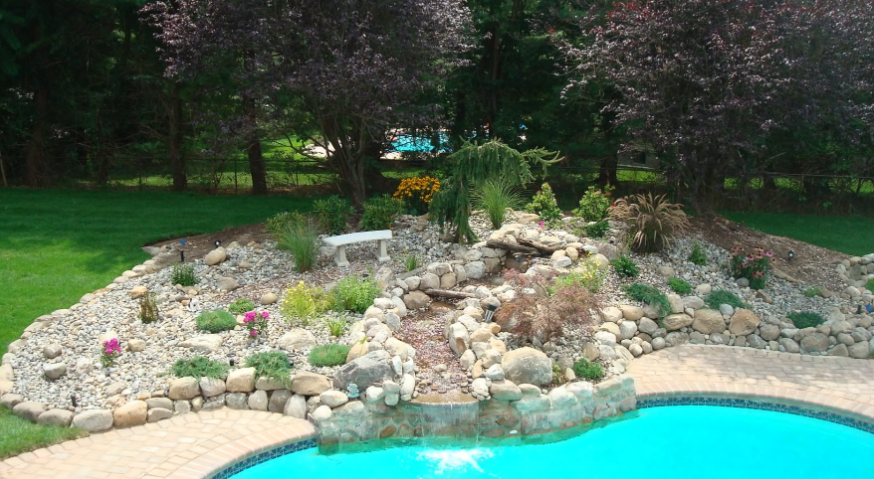 A backyard pool with a rock waterfall feature and surrounding landscaping.