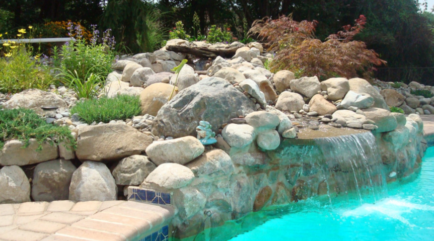 Waterfall feature with rocks and plants beside a swimming pool, water cascading into the turquoise water.