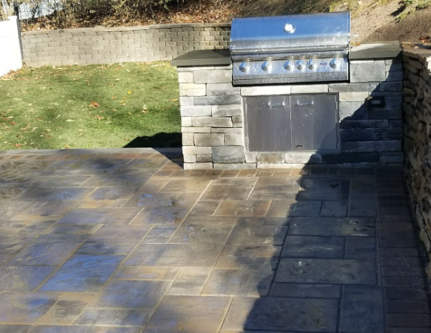 Patio with built-in grill and brick pavers. Grill station is gray stone, with a stainless steel grill.