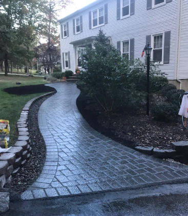 Brick paved walkway curves towards a two-story house with green lawn.