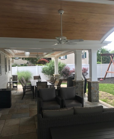Patio with seating, dining table, fans, and a light-colored wood ceiling.