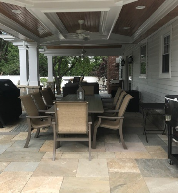 Covered patio with dining table and chairs, on stone tile flooring. Ceiling fan and recessed lighting visible.