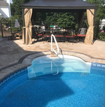 Pool with steps and handrails, shaded by a gazebo with tan curtains; outdoor setting.