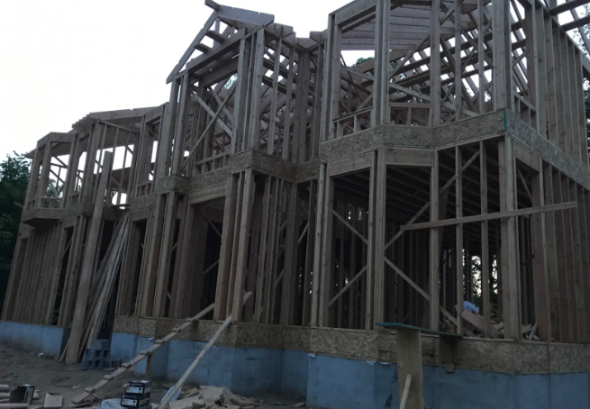 Wooden house frame under construction against a cloudy sky.
