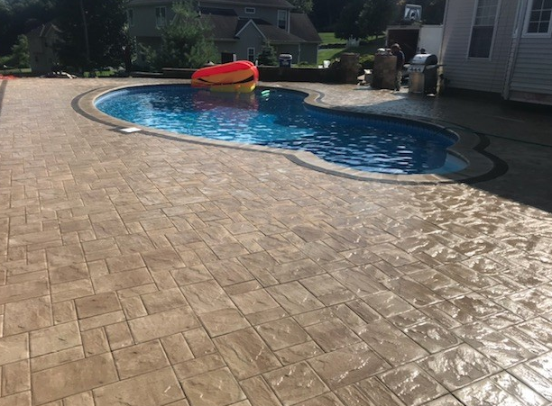 Pool area with a kidney-shaped pool, patterned concrete patio, and an inflatable raft.