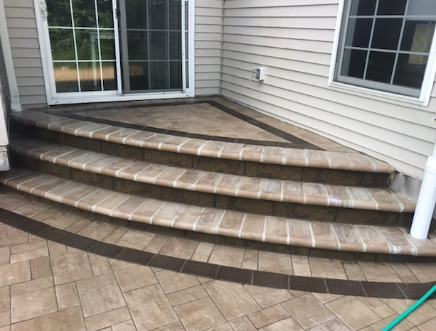 Brick patio with three steps leading to a sliding door, bordered with dark brown bricks.