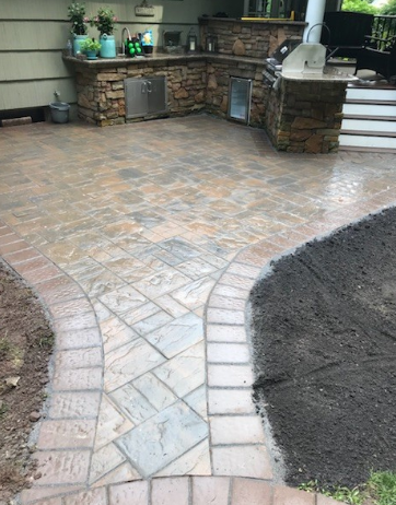 Outdoor kitchen with stone counters, built-in grill, and stamped concrete patio with decorative walkway.