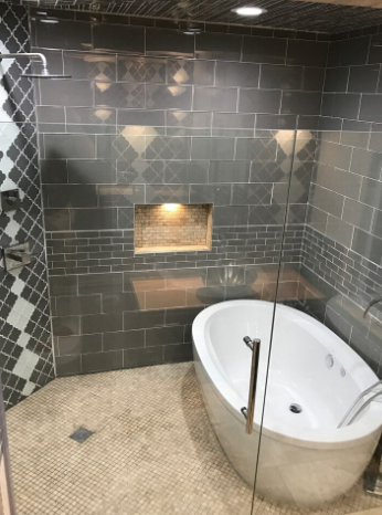 Bathroom with gray tile walls, a built-in tub, and a glass shower door.