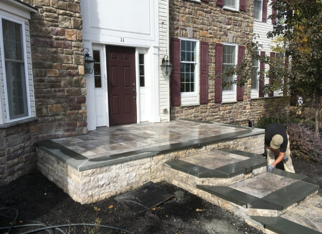Stone front steps leading to a house entrance. A person works on the steps.
