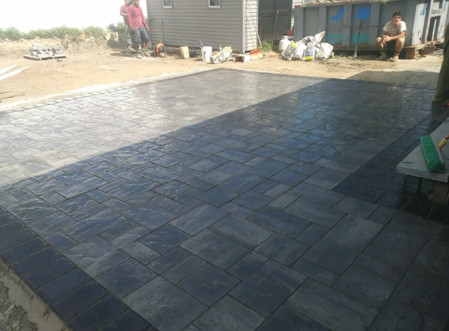 Newly installed dark gray patio pavers with a darker border. A person stands nearby.