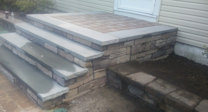 Stone steps and landing leading to a building's entrance. The steps and landing have a multi-tone color scheme.