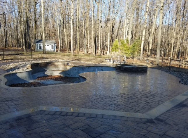 Patio with pool-like structure and fire pit, surrounded by trees.
