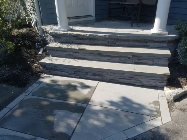 Stone steps lead up to a porch with white columns. The surrounding walkway is also stone.