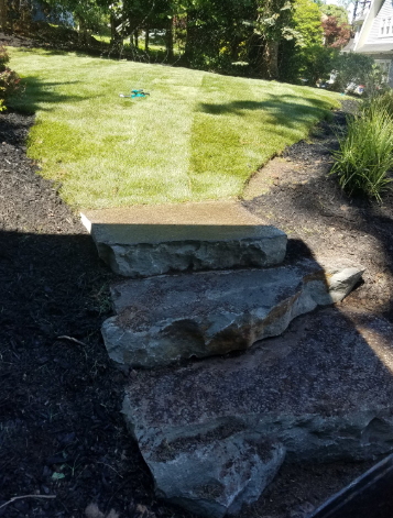 Stone steps leading up a sloped yard with fresh mulch and grass.