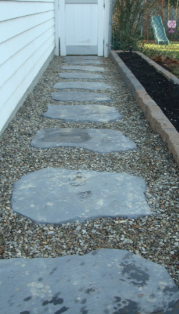 Stone pathway leading to a white door, surrounded by gravel and a garden bed with dark mulch.