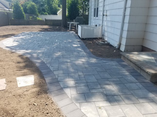 Paver patio in backyard with curved edges, next to a white house.