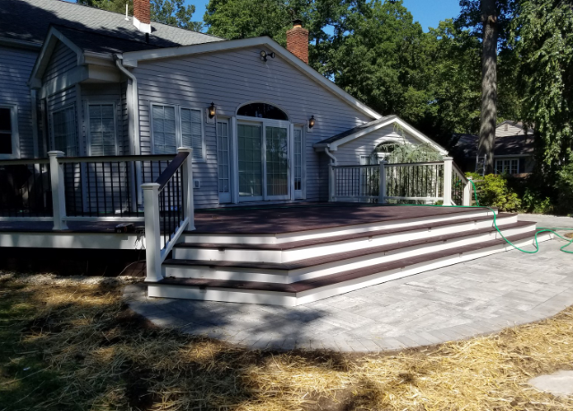 Backyard deck with dark brown boards, white railing, and curved concrete patio.