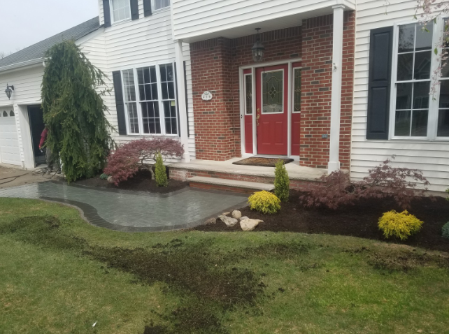 A house with a red front door, brick accents, and a landscaped front yard with freshly mulched beds and small shrubs.