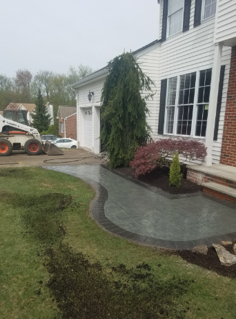 Paver walkway in front of a white house with a landscaped yard and a Bobcat machine on the lawn.