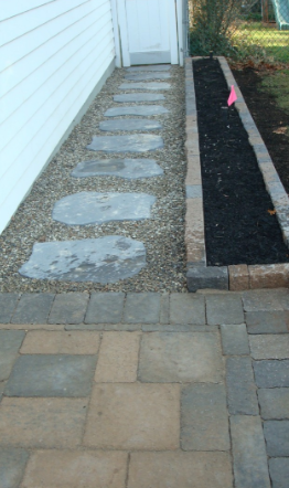 Stone pathway leading to a white door, with a gravel bed and flower bed alongside.