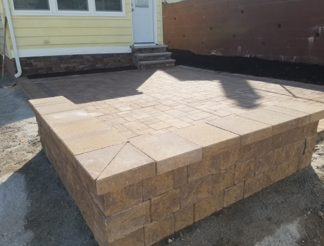Brown brick patio with retaining wall, leading to a doorway and steps.