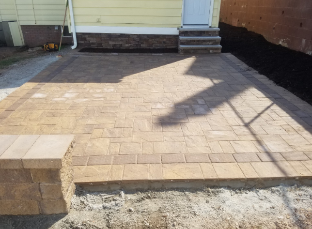 Brick patio with border adjacent to a building. Steps lead up to a doorway.