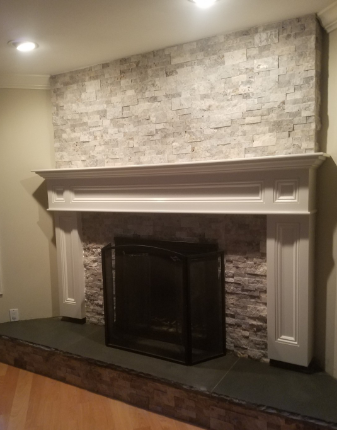 Fireplace with white mantle and stacked stone surround, black screen, and dark hearth.