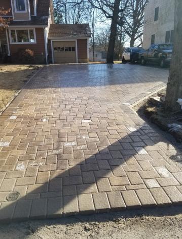 Brick paver driveway in front of a house and garage; a tree casts a shadow.