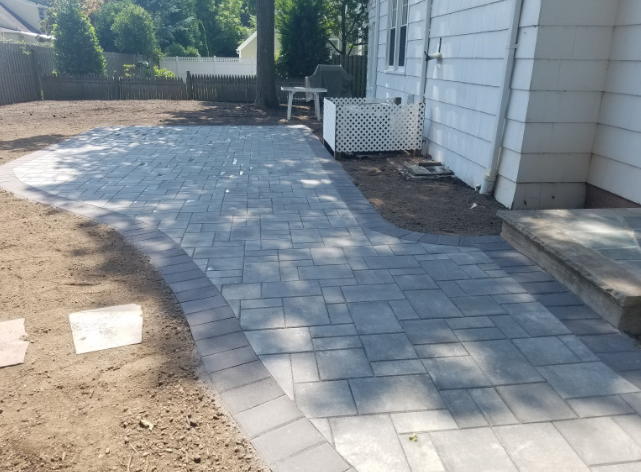 A gray paver patio and walkway adjacent to a white house.