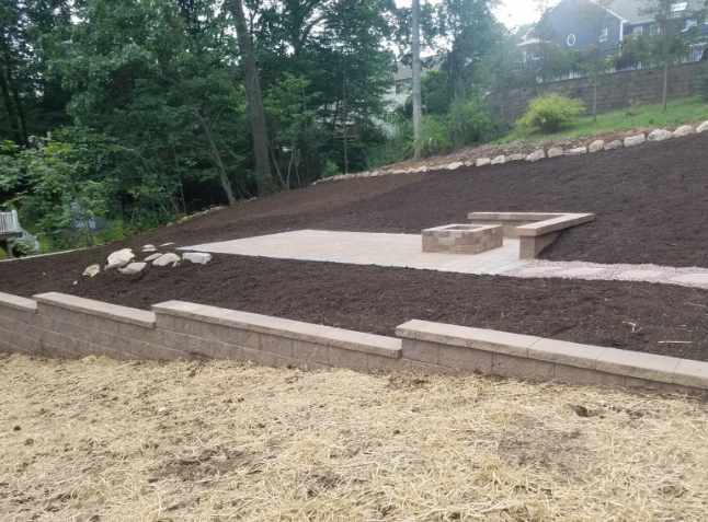 Landscaped hillside with retaining walls, mulch, and a stone fire pit area.