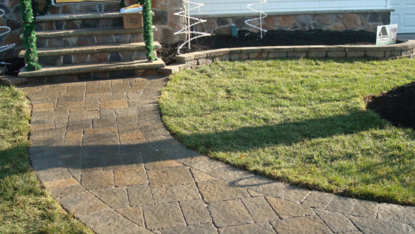 Stone walkway curves through grass toward steps, leading to a building's entrance.