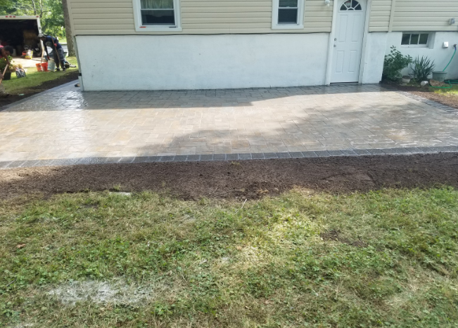 Newly poured concrete patio next to a house with gravel border and green grass.