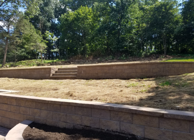 Stone retaining walls with steps, brown grass, and trees in background.