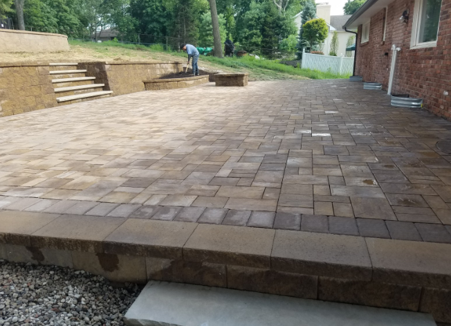 Brick patio with retaining wall, stairs, and person working on the top of the slope.