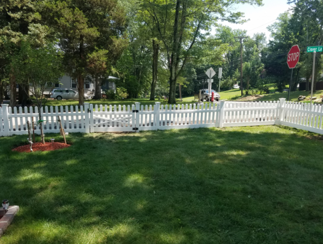 White picket fence surrounding a grassy yard near a street with a stop sign.