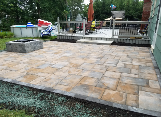 Stone patio with a fire pit and deck in a backyard.