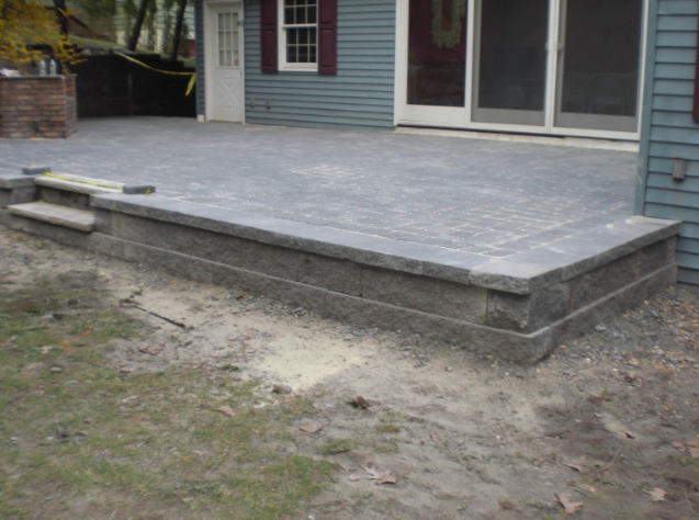 Raised patio with steps, gray pavers, and a blue house.