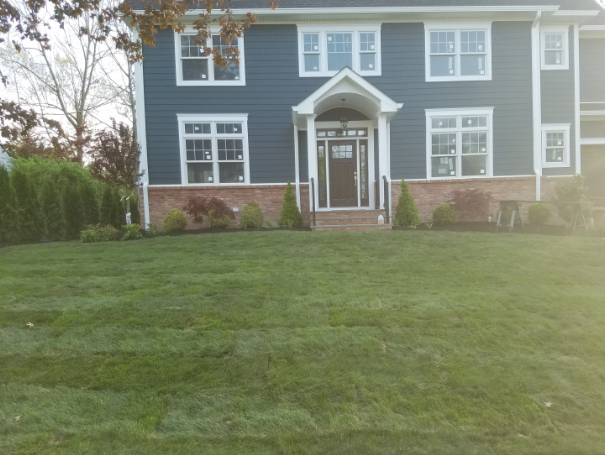 Two-story house with dark blue siding, white trim, and a brick base; green lawn.