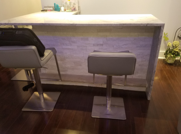 Two gray bar stools at a white marble countertop with white brick facade.