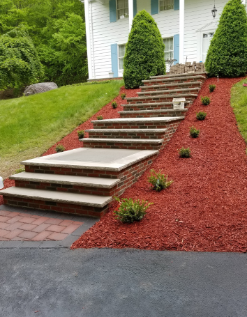 Brick steps leading up to a white house, surrounded by red mulch and greenery.