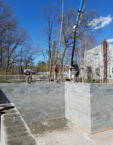 Construction workers pouring concrete into a cinder block foundation, using a pump. Sunny day.