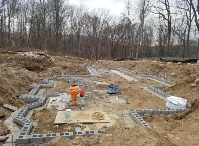 Foundation construction site with cinder block walls, dirt, trees in background, and construction equipment.