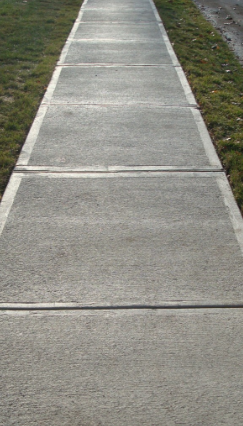 Concrete sidewalk with rectangular sections, flanked by grass.